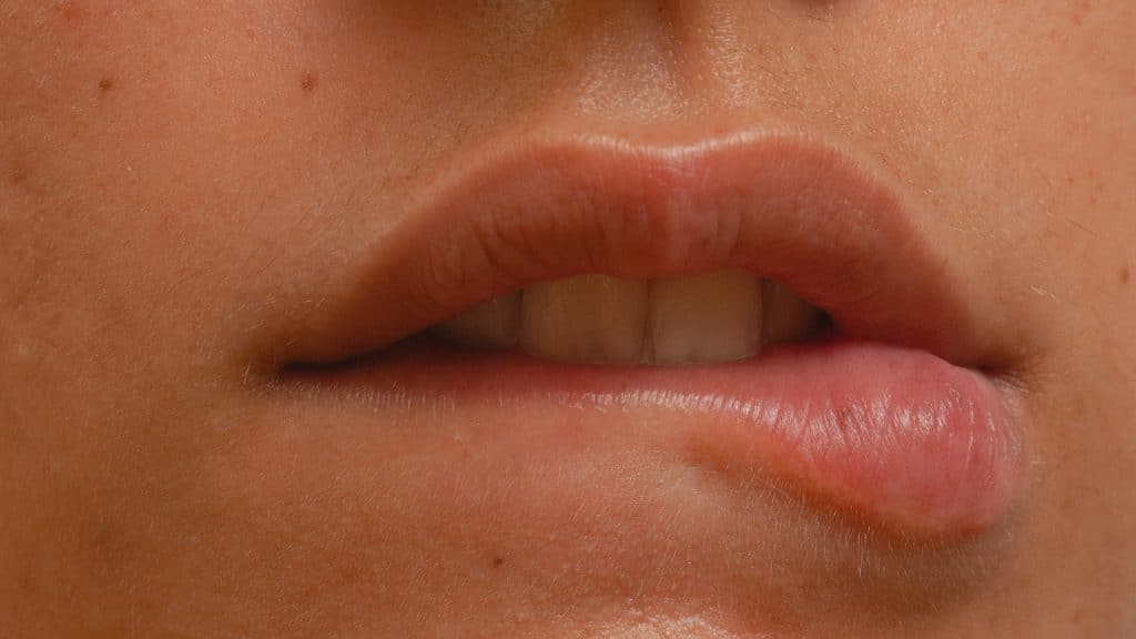 Extreme close-up of a person gently biting their lower lip with their teeth.