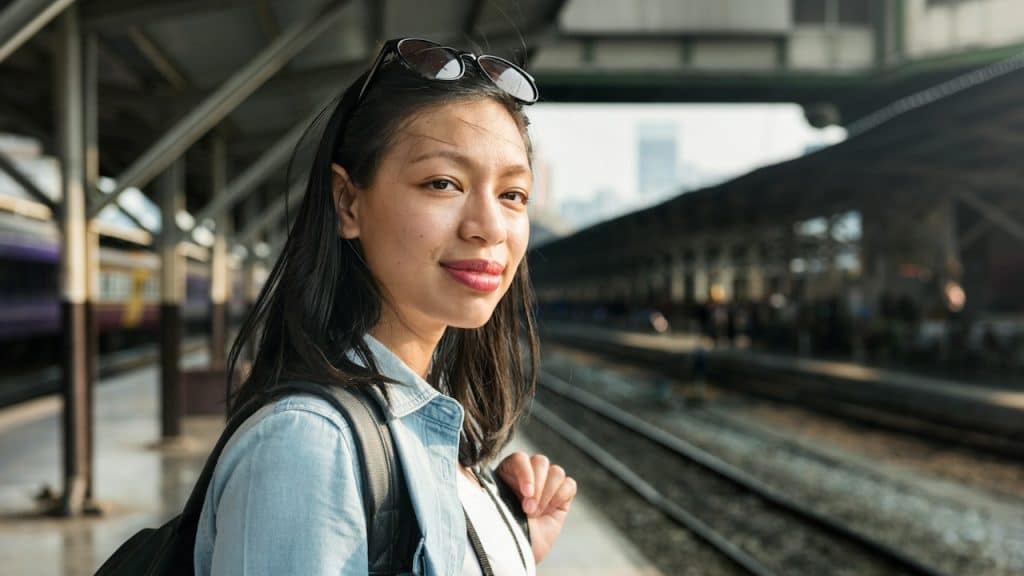 A woman wearing her sunglasses on her head looking at the camera while standing at a train station.