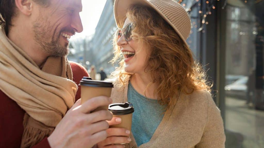 A smiling couple holding takeaway coffee cups while walking outdoors.