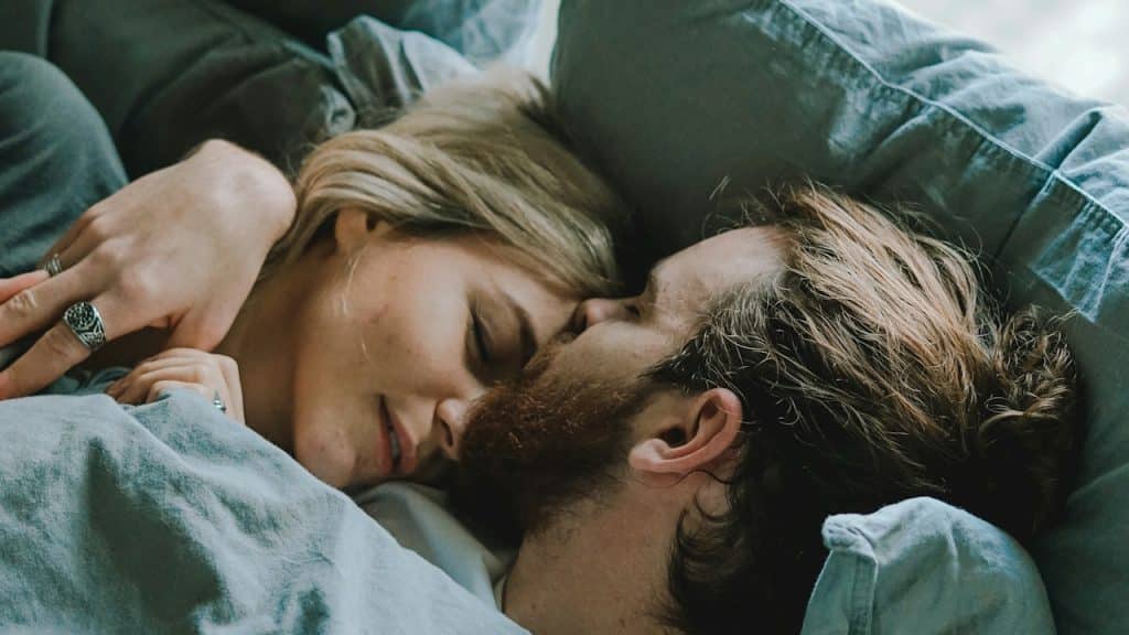 A man kissing a woman’s forehead as they lie in bed.