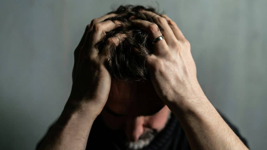 A close-up shot shows a man’s hands clutching his hair with his head tilted down.