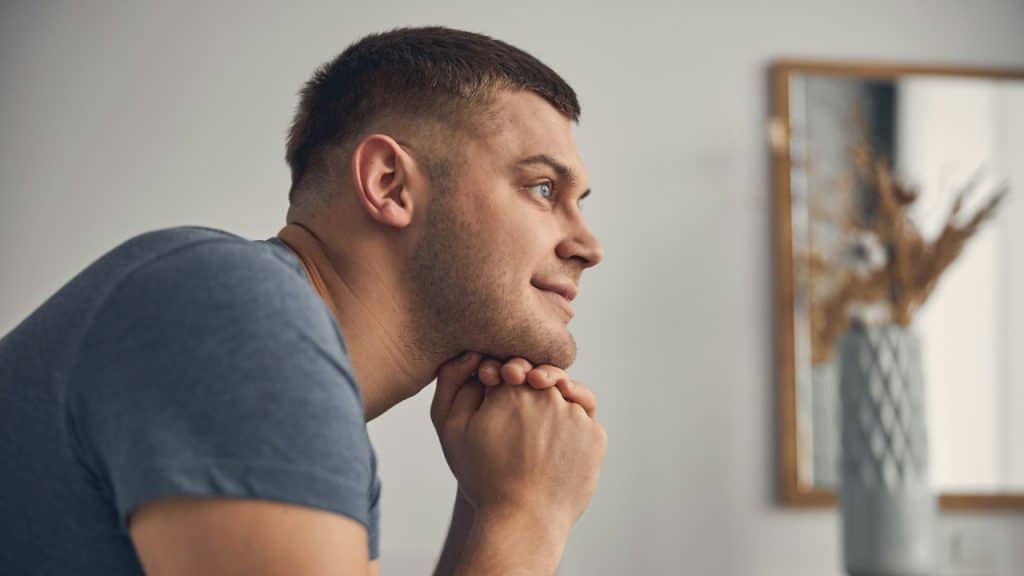A man with short hair rests his chin on his hands and looks away.