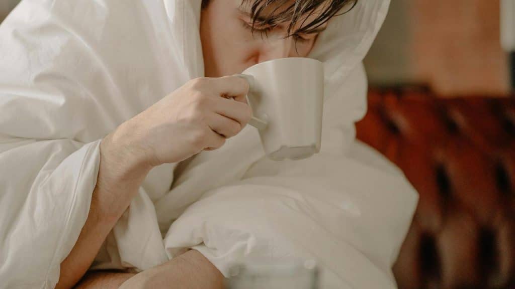 A person drinking from a mug while wrapped in a blanket.