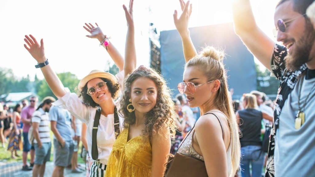 A group of friends dancing and cheering at an outdoor music festival.