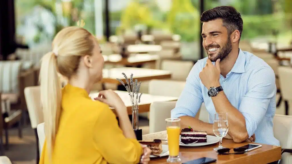 A happy man talking to his girlfriend while having dessert in a cafe.