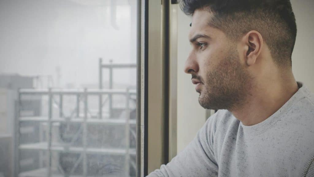 A man gazes out a window with an industrial scene visible outside.