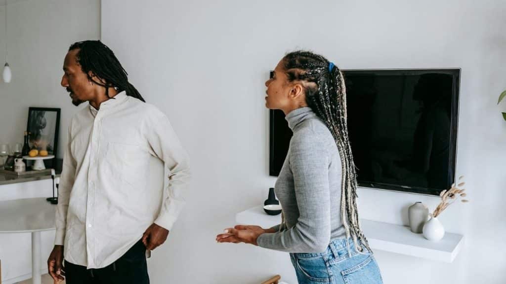 A woman with braided hair gestures toward a man who is walking away from her.