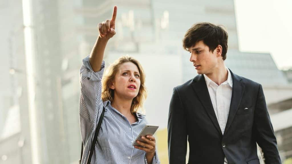A woman in a striped shirt points upward while a man in a suit looks on.