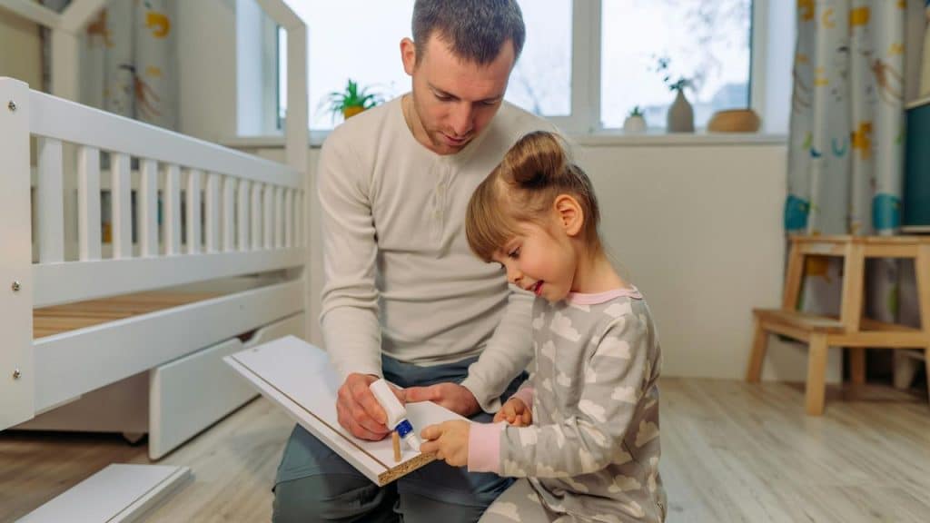A father and daughter assembling furniture in a bedroom.