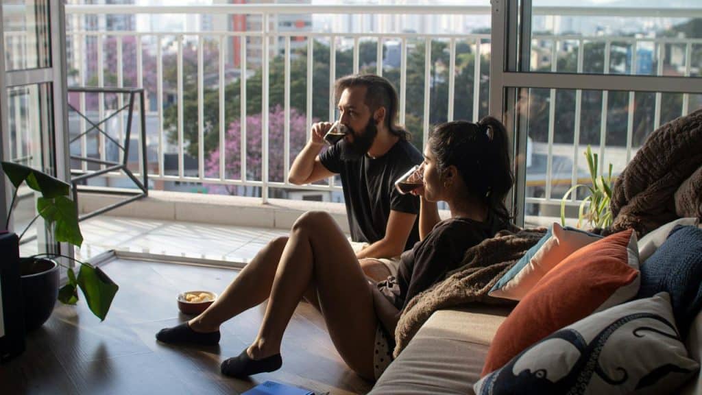A couple sitting on the floor by a balcony, sipping coffee in morning light.