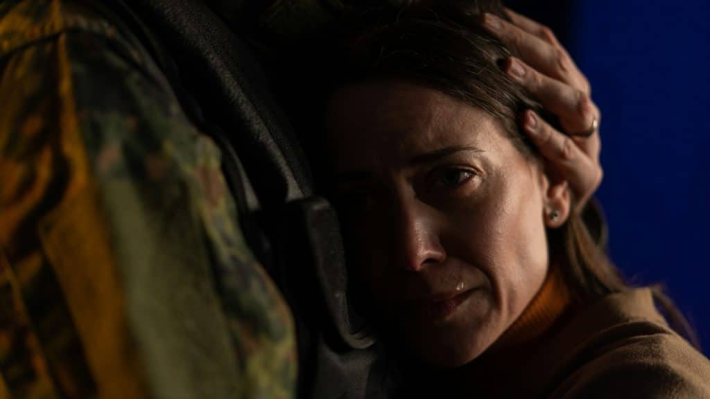 A woman rests her head against a person in uniform while a hand touches her hair.