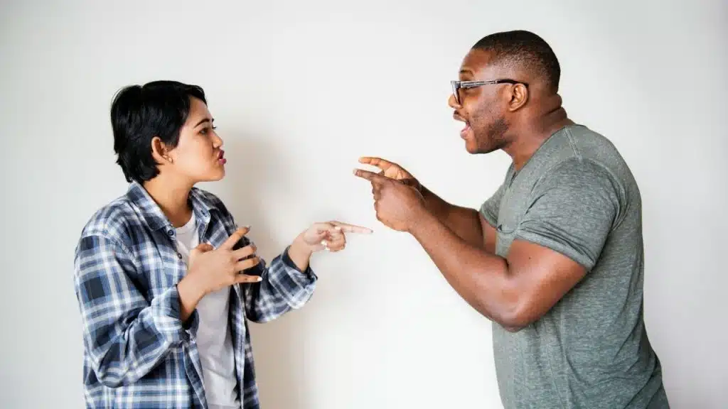 A man and woman point at each other while speaking intensely against white background.