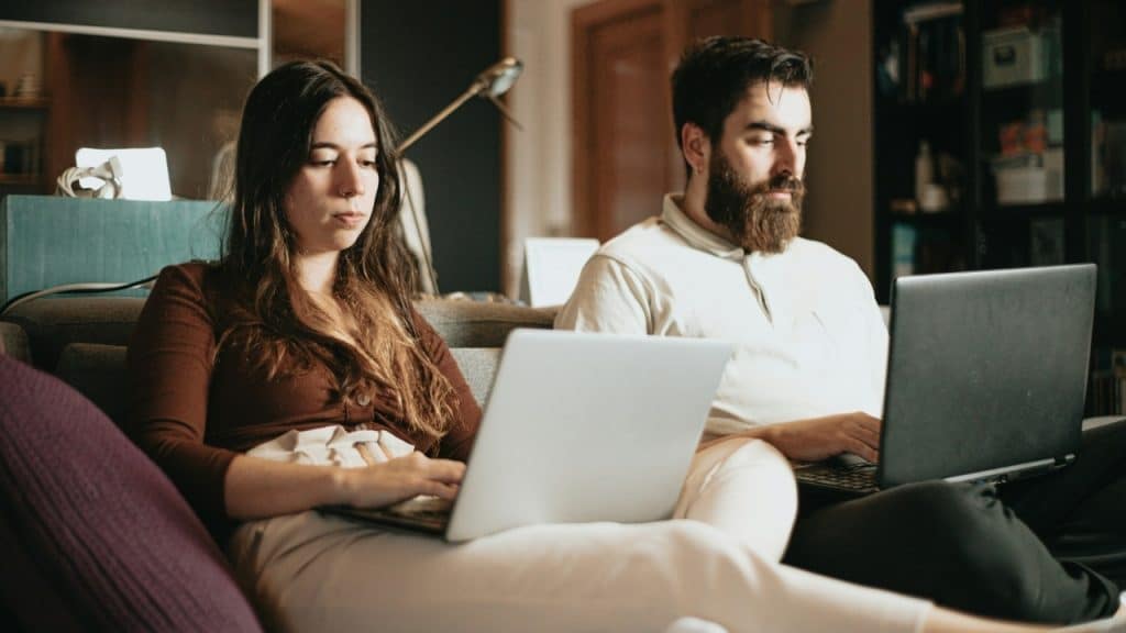 A woman with long dark hair and a bearded man sit together using separate laptops.