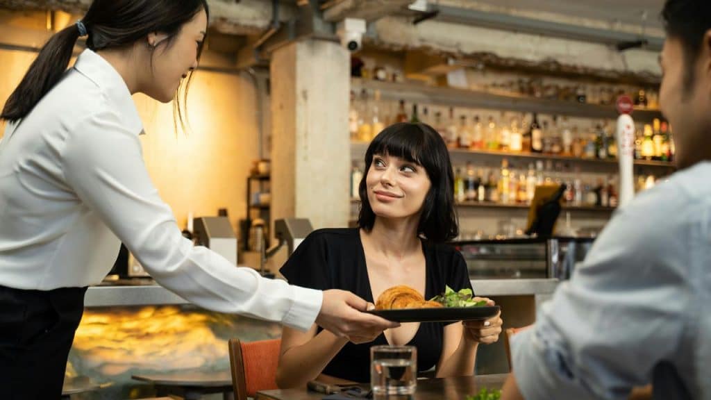 A server placing a plate of food in front of a woman at a restaurant table.