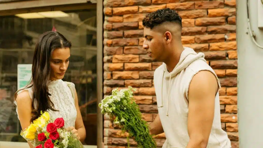 A man with a fade haircut holds green flowers while standing near a woman holding roses.