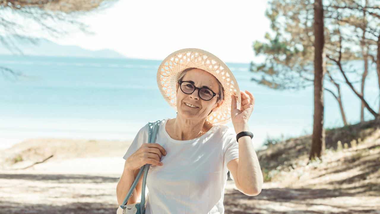 An older woman wearing a hat at the beach.