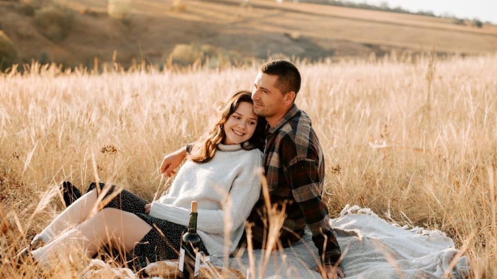 A woman lying in the lap of her husband while they are sitting in a field.