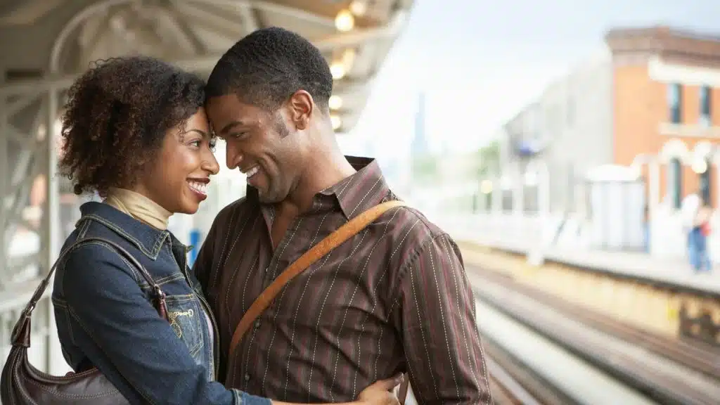 A couple smiling closely together on a train platform.