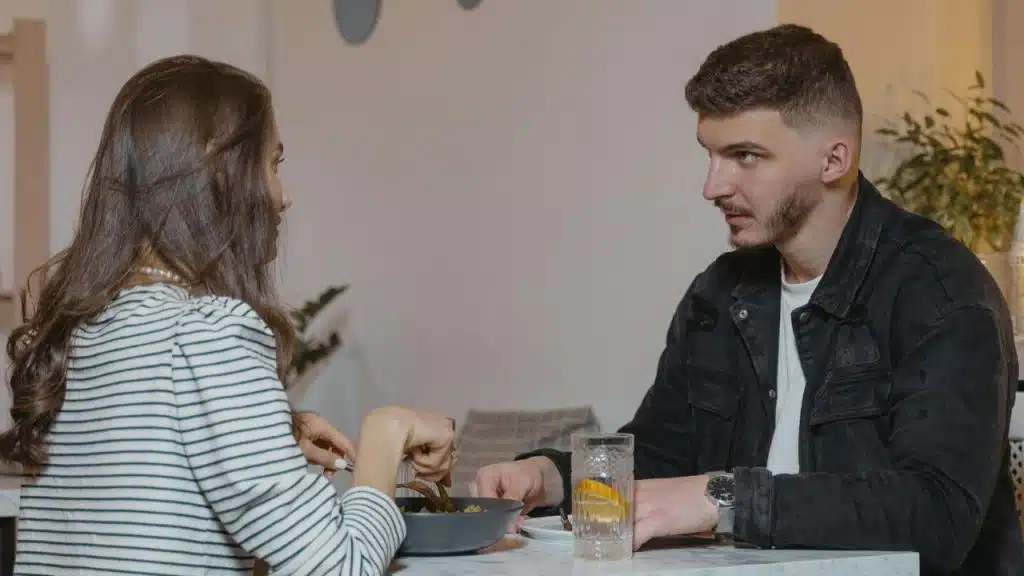 A man and woman sit at a table together while eating and having a conversation.