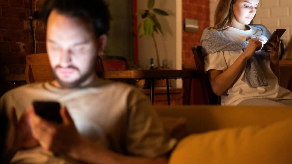 A couple sitting apart indoors, each focused on a phone.