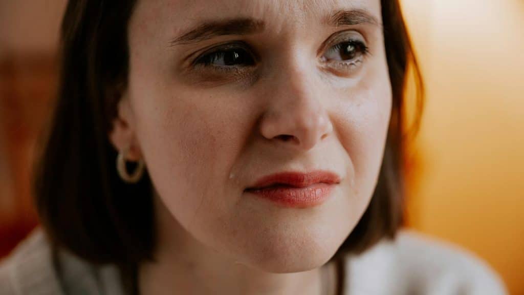 A close-up of a woman with teary eyes and a solemn expression in warm light.