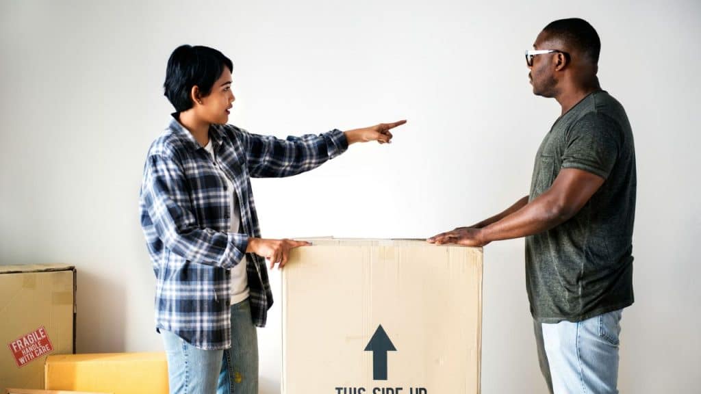 A woman points while she and a man stand next to a large cardboard box.