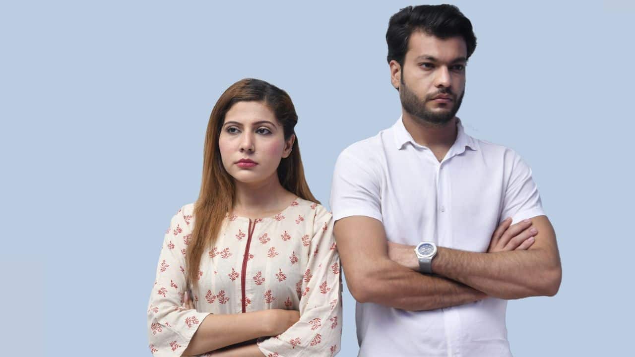 A man and woman stand side-by-side with arms crossed, looking in different directions.