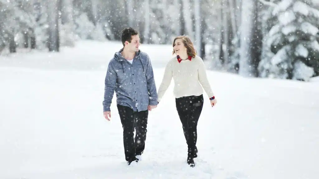 A man and a woman holding hands while walking in snowfall.