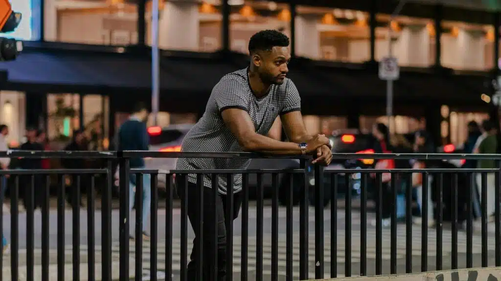 A man leaning on a railing in a city at night.