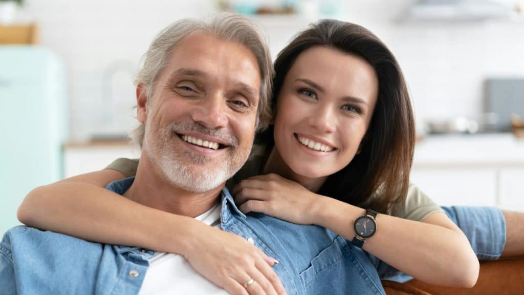 A man and woman smile closely together while the woman rests her arm on his shoulder.