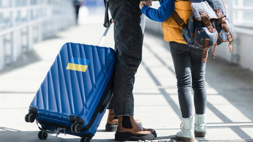 A person with a child holding a blue suitcase at an airport.