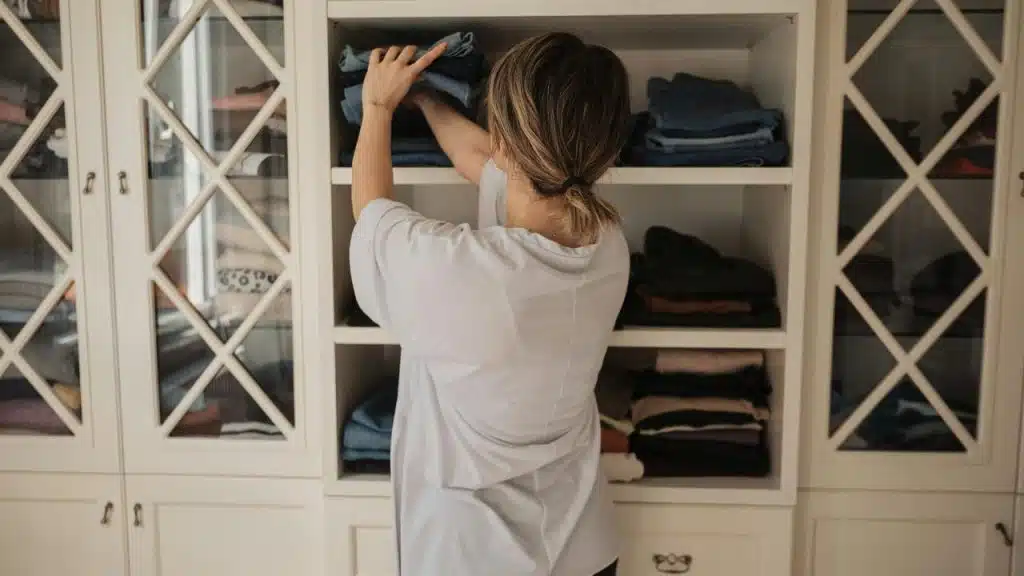 A person organizing folded clothes on shelves in a wardrobe.