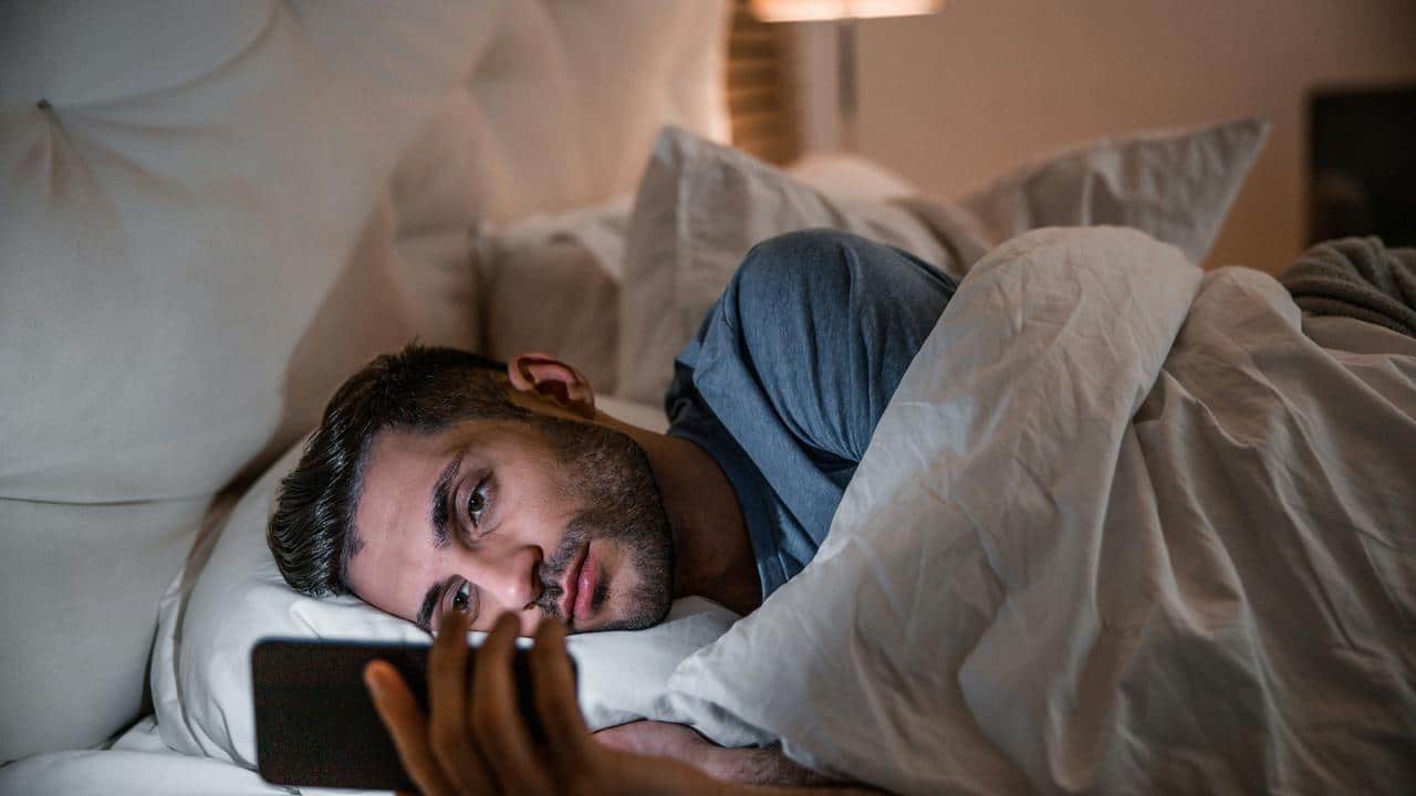 A man lying in bed at night looking at his smartphone.
