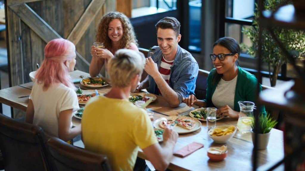 A group of five friends talks and laughs while sharing a meal at a table.