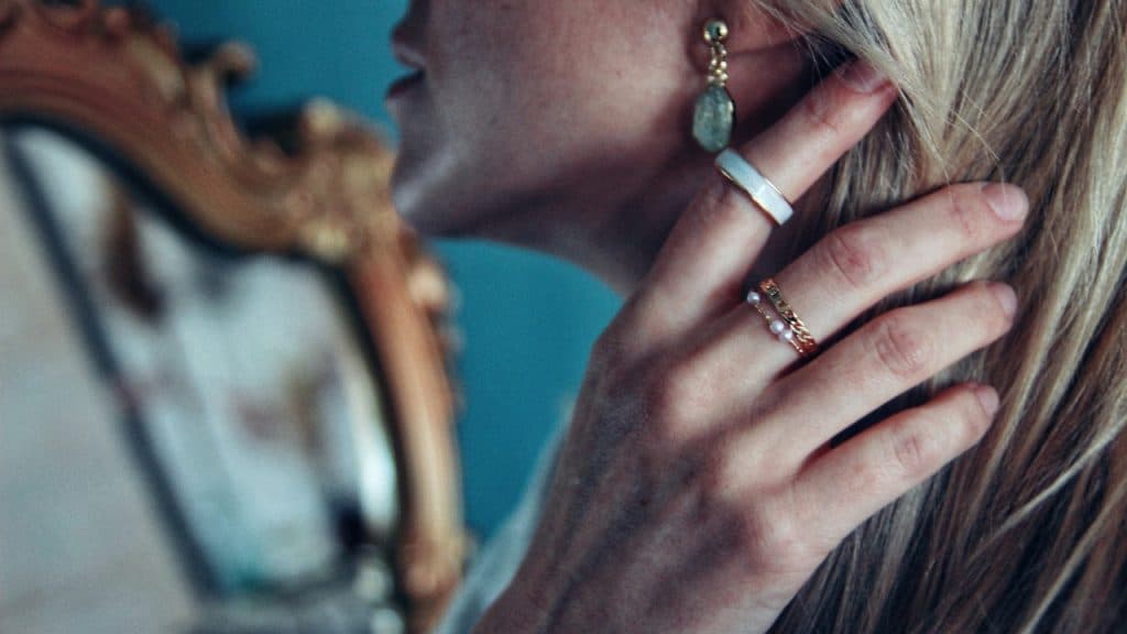 Close-up of a woman’s hand with rings tucking her blonde hair behind her ear.
