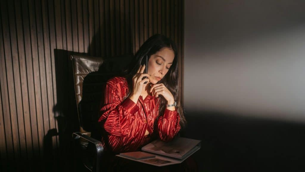 A woman talking on the phone while looking at a report in a dimly lit room.
