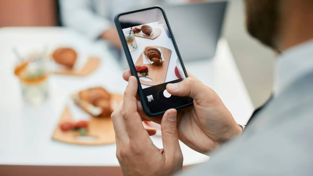 A person taking a photo of a croissant and strawberries with a smartphone.