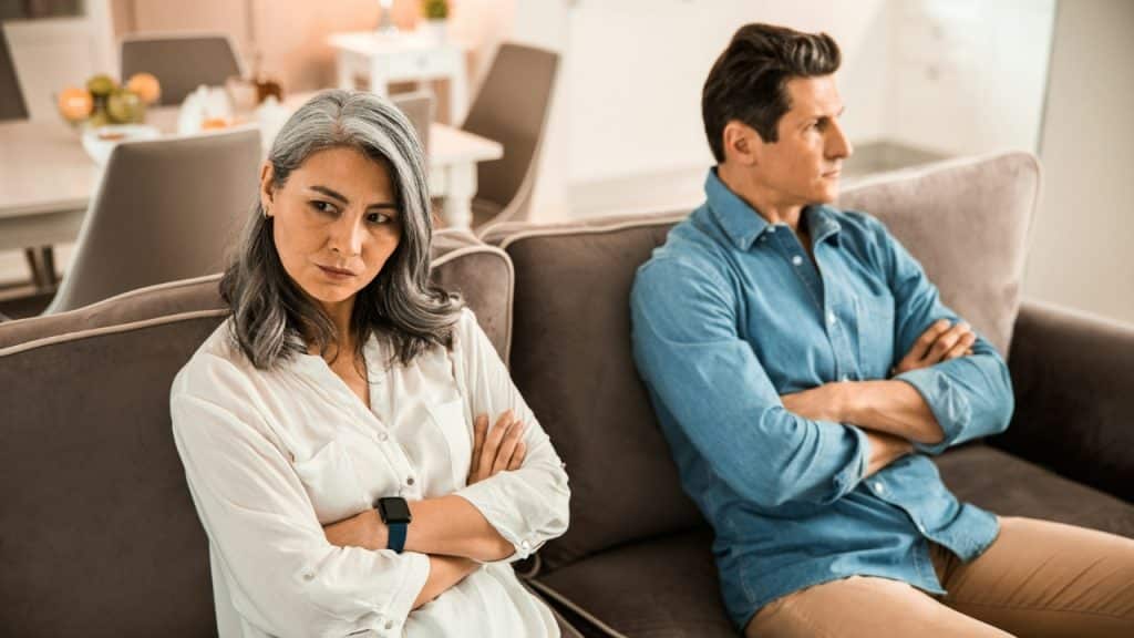 A man and woman sit on a couch with arms crossed while looking away from each other.
