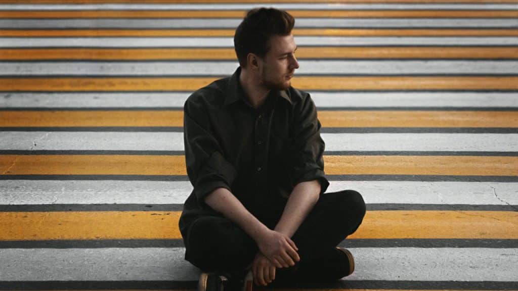 A man sitting cross-legged on striped steps, looking to the side.