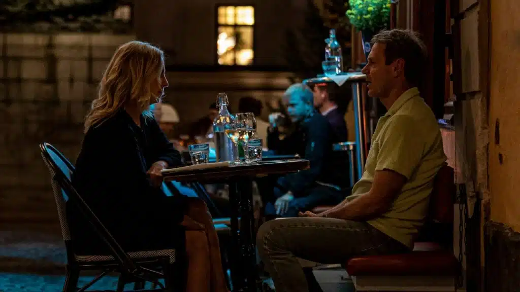 A man and a woman sit at an outdoor table at night, engaged in a conversation.