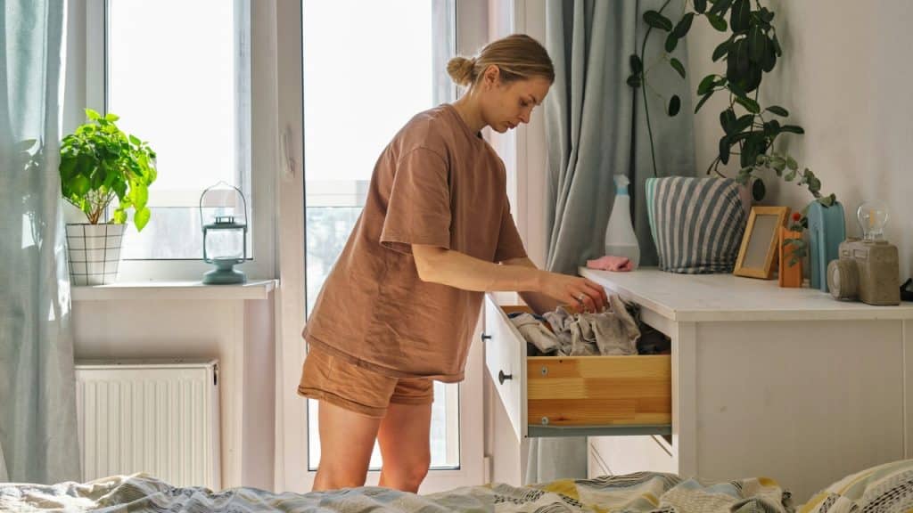 A woman in a brown outfit stands in a room while organizing clothes in a dresser.