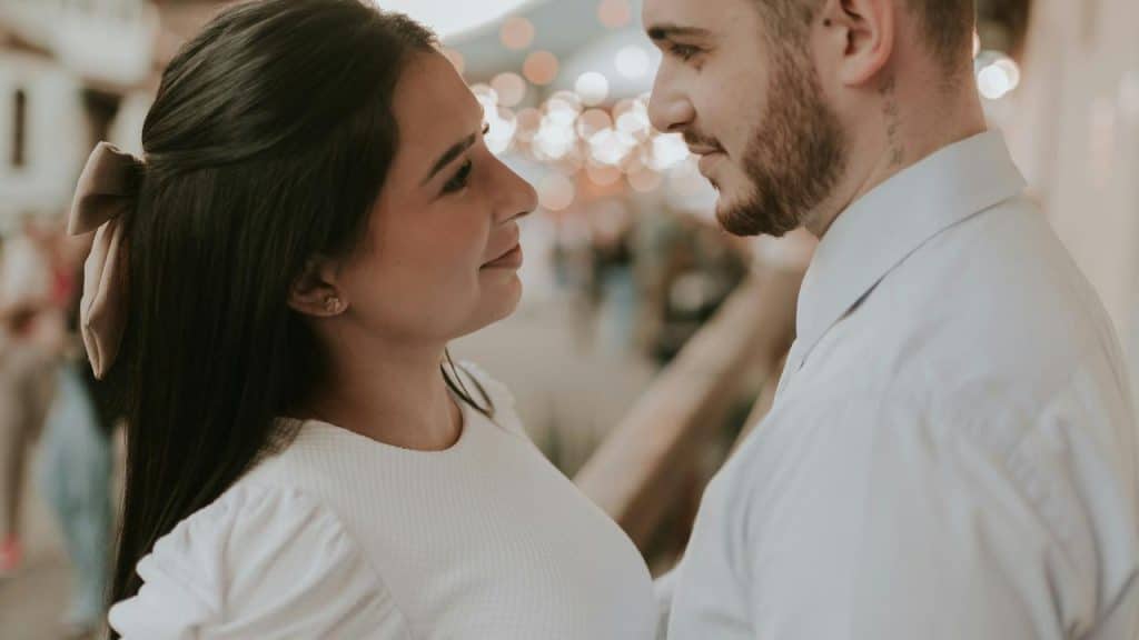 A couple gazing at each other closely in a softly lit outdoor setting.