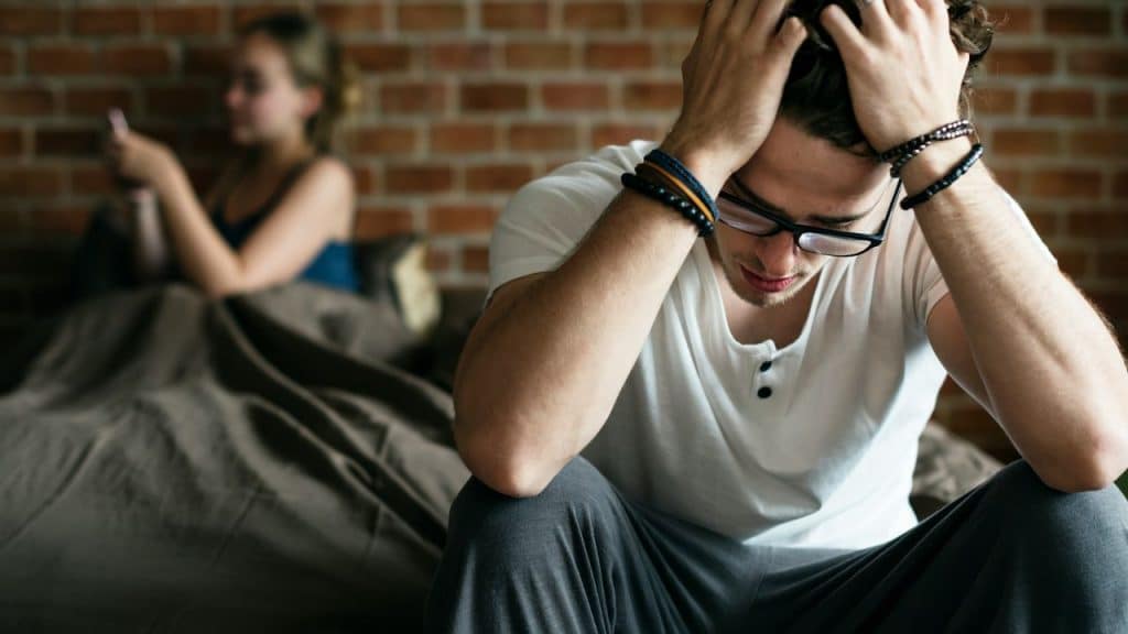 A man sits with his head in his hands while a woman sits in the background.
