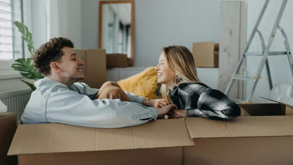 A smiling couple sitting inside cardboard boxes while moving into a new home.