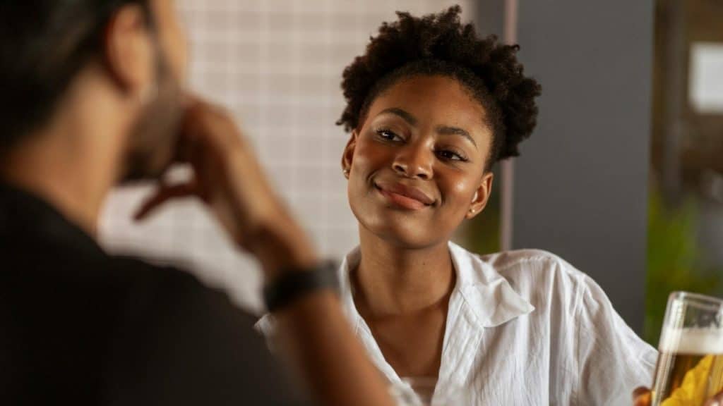 A woman with short curly hair smiles while looking at a man across from her.