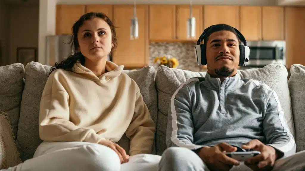 A man wearing headphones plays a video game while a woman sits beside him looking away.
