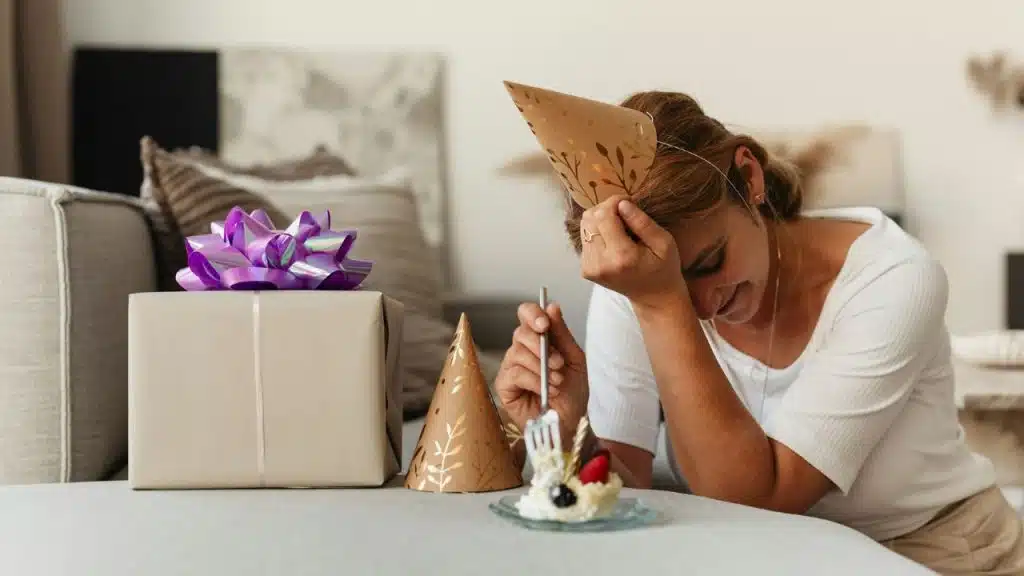 A woman wearing a party hat leans her head on her hand next to cake.