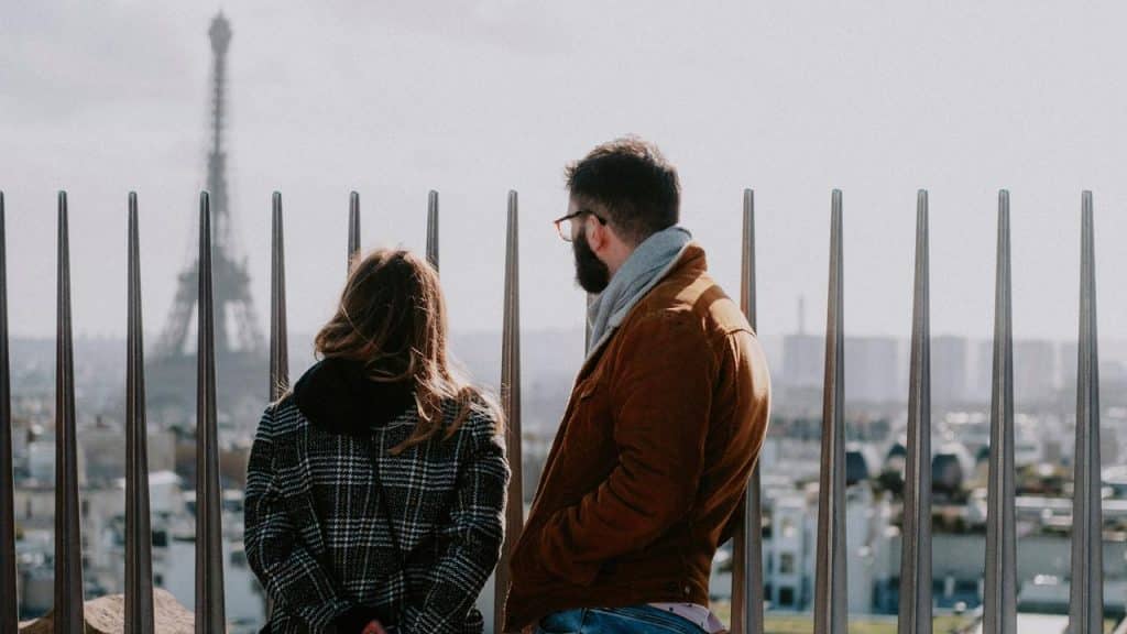 A couple standing together and looking out over a city with the Eiffel Tower in the distance.