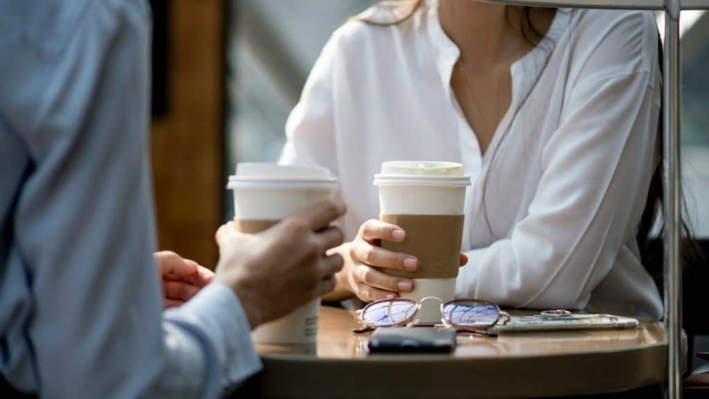 A close-up of two people holding takeaway coffee cups at a café table.