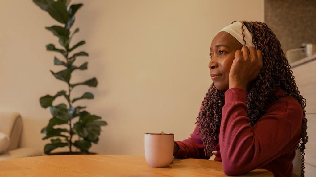 A woman sitting at a table with a mug, resting her head on her hand and looking ahead.